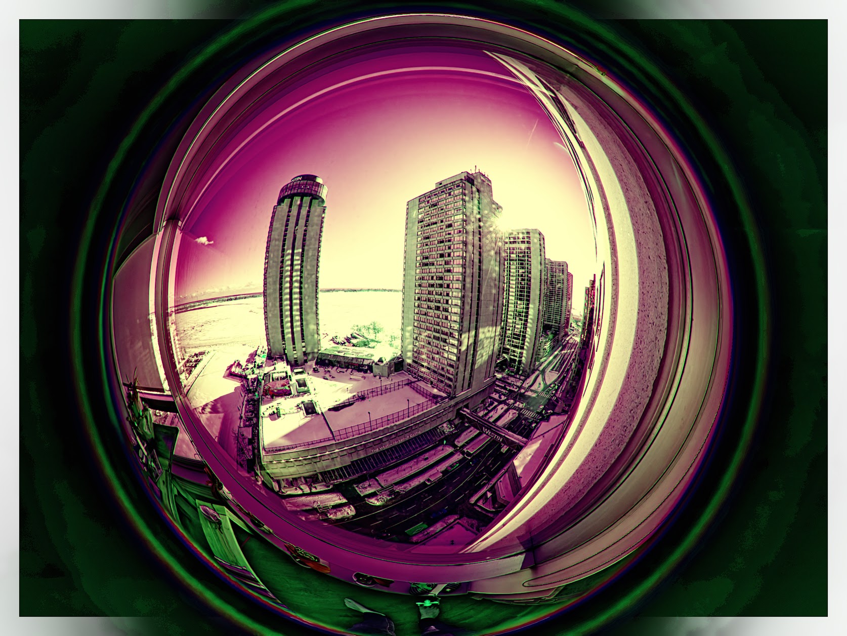 A circular fisheye photograph of the Toronto waterfront, the whole scene bent into a globe floating in a dark green rectangle. Highrise towers and the Westin lean outward from the centre, the frozen lake and a flared sun sit behind them, and the road and parked cars curve around the bottom edge. Colours are pushed to magenta sky and pale yellow light.